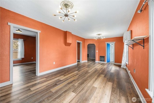 unfurnished living room with heating unit, arched walkways, an inviting chandelier, and dark wood finished floors