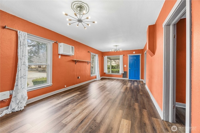 unfurnished living room featuring a notable chandelier, wood finished floors, baseboards, and a wall mounted AC