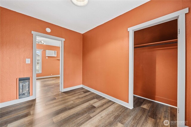 unfurnished bedroom featuring heating unit, a closet, baseboards, and wood finished floors