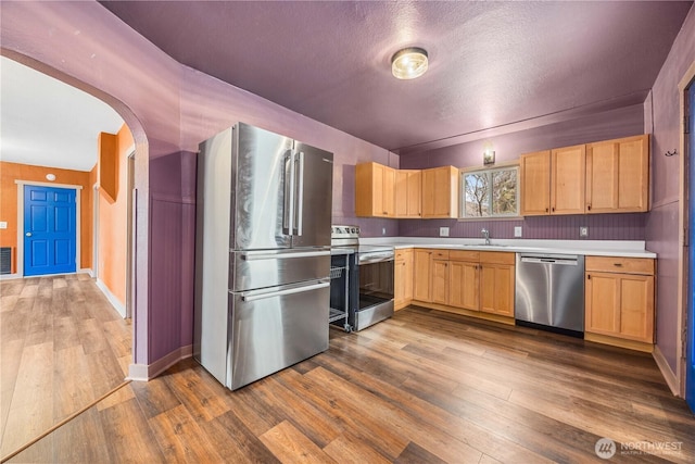 kitchen with light brown cabinets, arched walkways, a sink, stainless steel appliances, and light countertops