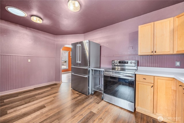 kitchen featuring light brown cabinetry, appliances with stainless steel finishes, wood finished floors, and arched walkways