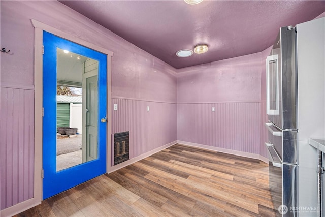 unfurnished room with heating unit, wood finished floors, and a wainscoted wall