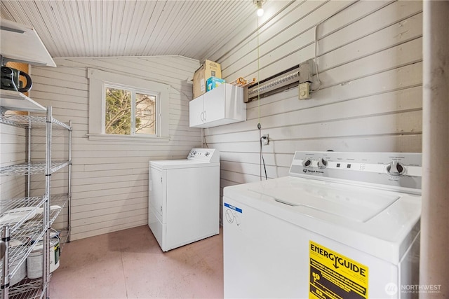 washroom featuring washer and dryer, cabinet space, and wood walls