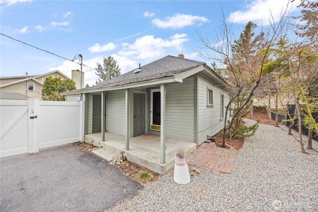 exterior space with a gate, fence, roof with shingles, a chimney, and a patio area