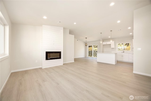 unfurnished living room featuring lofted ceiling, recessed lighting, a fireplace, light wood finished floors, and baseboards