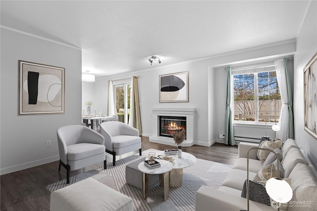 living area with wood finished floors, baseboards, a textured ceiling, crown molding, and a brick fireplace