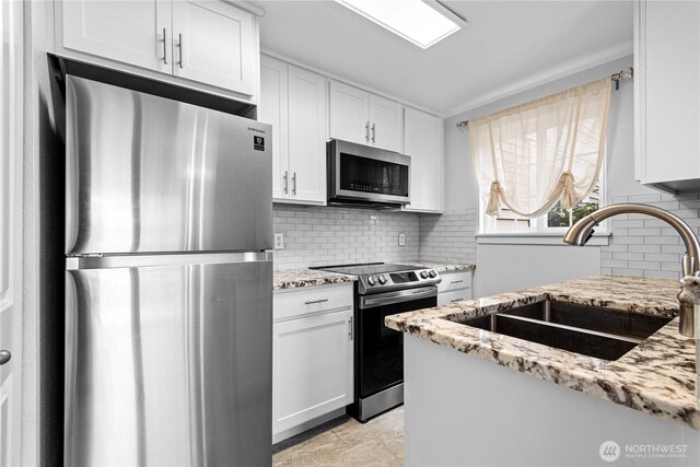 kitchen featuring a sink, backsplash, white cabinetry, stainless steel appliances, and light stone countertops