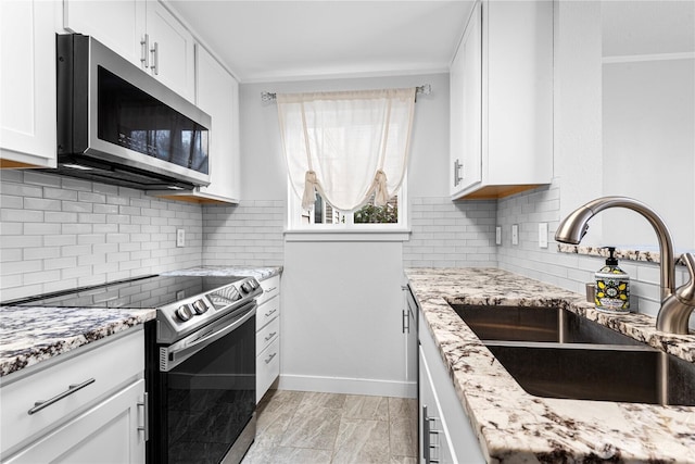 kitchen featuring a sink, light stone counters, appliances with stainless steel finishes, and white cabinets