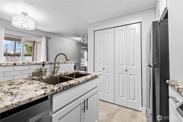 kitchen with light stone counters, freestanding refrigerator, a sink, white cabinets, and tasteful backsplash