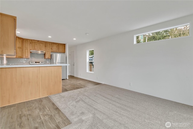 kitchen with under cabinet range hood, plenty of natural light, backsplash, and freestanding refrigerator