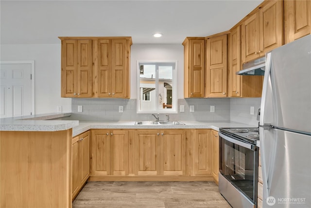 kitchen with a sink, under cabinet range hood, stainless steel appliances, a peninsula, and light countertops