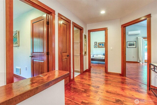 corridor with an AC wall unit, wood finished floors, baseboards, and recessed lighting