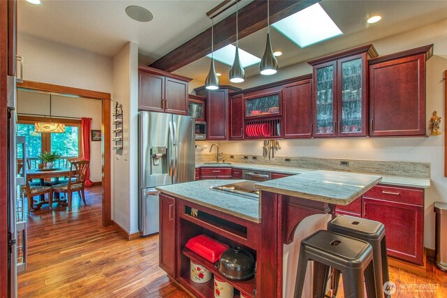 kitchen featuring appliances with stainless steel finishes, a sink, decorative light fixtures, light wood-style floors, and light stone counters