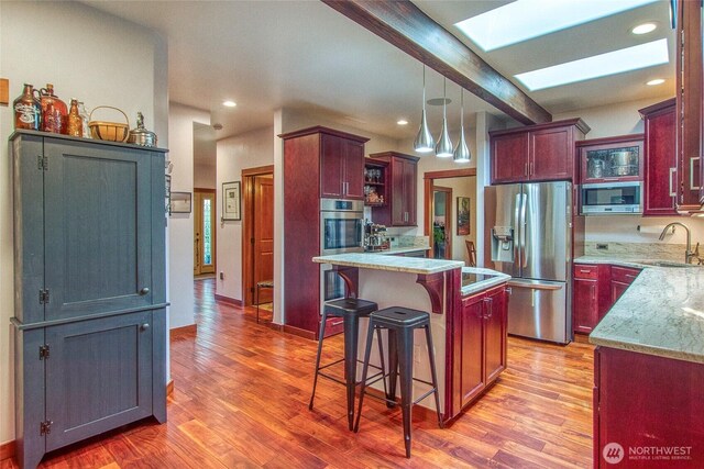kitchen featuring appliances with stainless steel finishes, a sink, a skylight, light wood-type flooring, and reddish brown cabinets