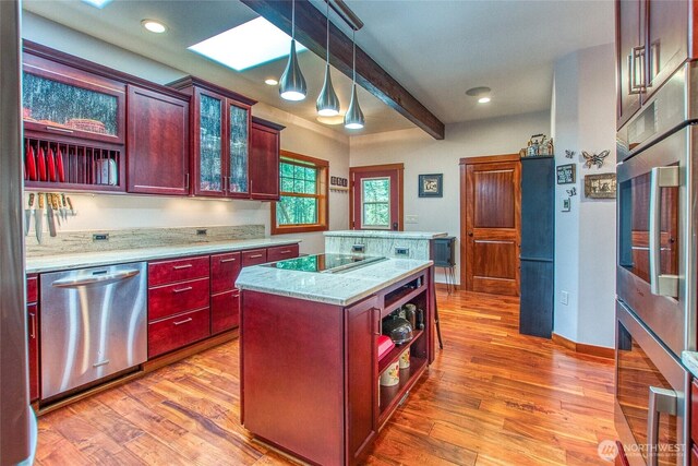 kitchen featuring appliances with stainless steel finishes, a skylight, a kitchen island, reddish brown cabinets, and light wood-style floors