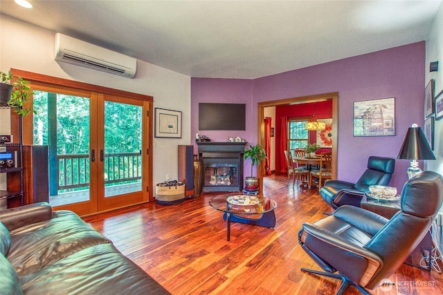 living area with a wall unit AC, french doors, wood finished floors, and a glass covered fireplace
