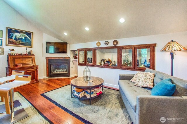 living area with a glass covered fireplace, recessed lighting, wood finished floors, lofted ceiling, and baseboards