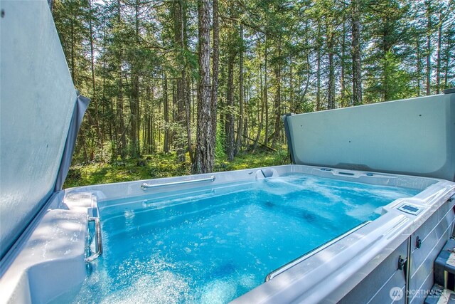 view of pool with a hot tub and a view of trees