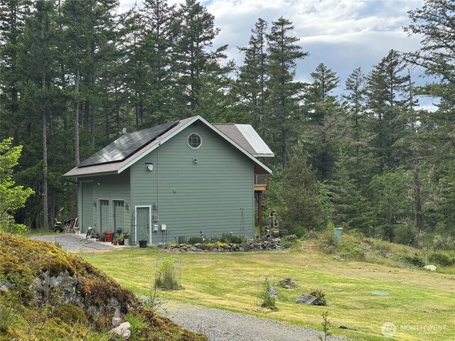 view of side of property featuring solar panels, a yard, and a forest view