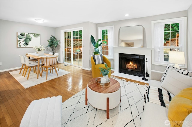 living room featuring recessed lighting, baseboards, wood-type flooring, and a lit fireplace