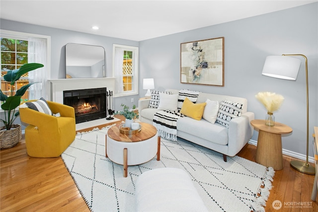 living area with a fireplace with flush hearth, recessed lighting, baseboards, and wood finished floors