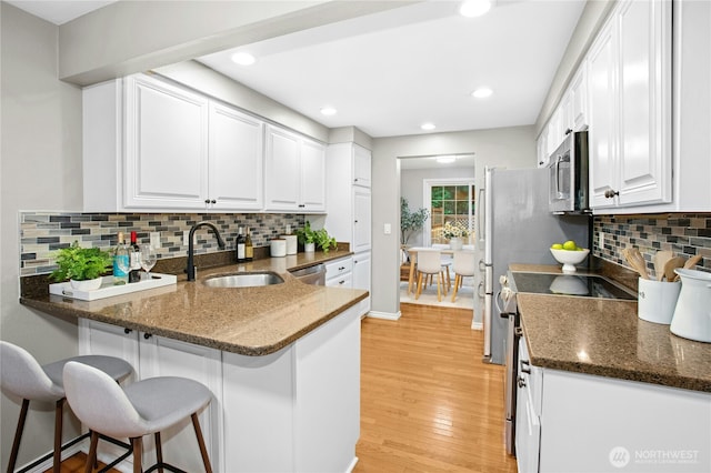 kitchen featuring light wood-type flooring, a sink, white cabinetry, stainless steel appliances, and a breakfast bar area