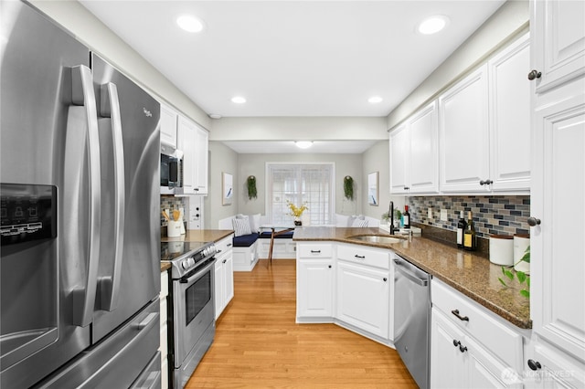 kitchen featuring a peninsula, a sink, stainless steel appliances, white cabinets, and light wood-type flooring