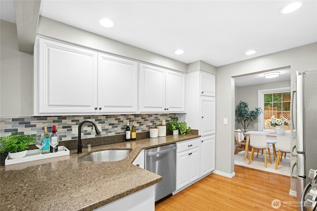 kitchen with light wood finished floors, a sink, decorative backsplash, white cabinets, and appliances with stainless steel finishes