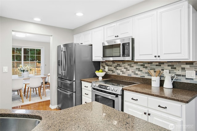 kitchen with backsplash, stainless steel appliances, and dark stone countertops