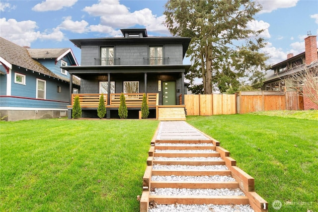 view of front of house with a front yard, a balcony, and fence