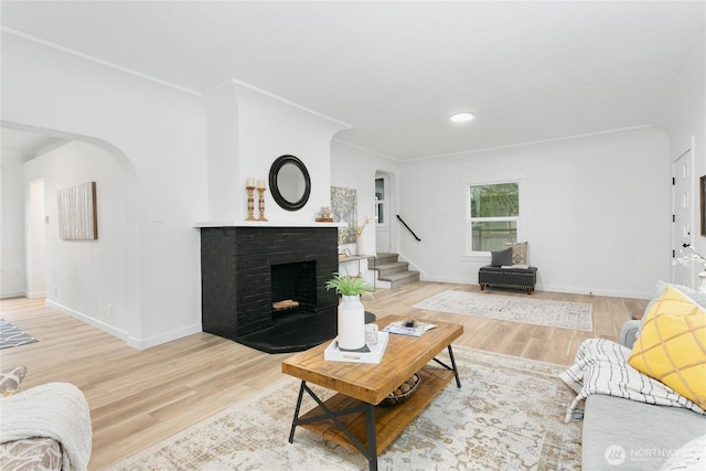 living area with a brick fireplace, wood finished floors, arched walkways, and baseboards