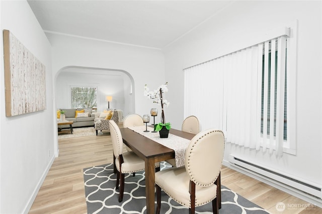 dining space with a baseboard heating unit, baseboards, arched walkways, and light wood finished floors