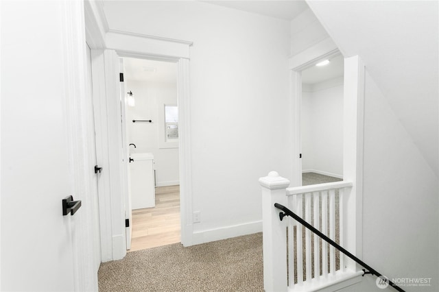 hall featuring an upstairs landing, baseboards, and carpet floors