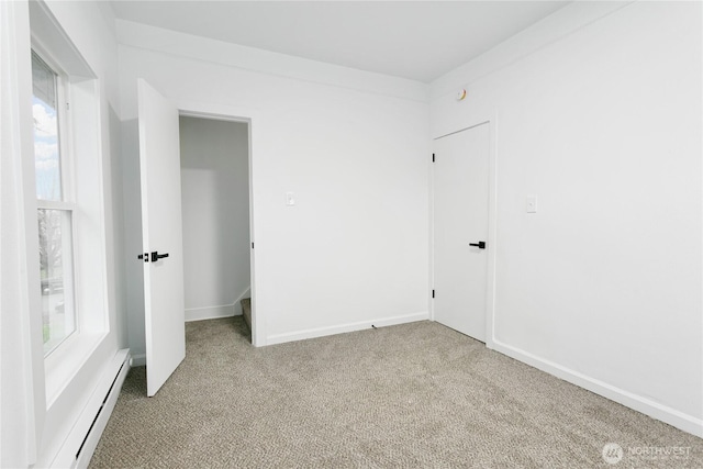 unfurnished bedroom featuring a baseboard heating unit, baseboards, and light colored carpet