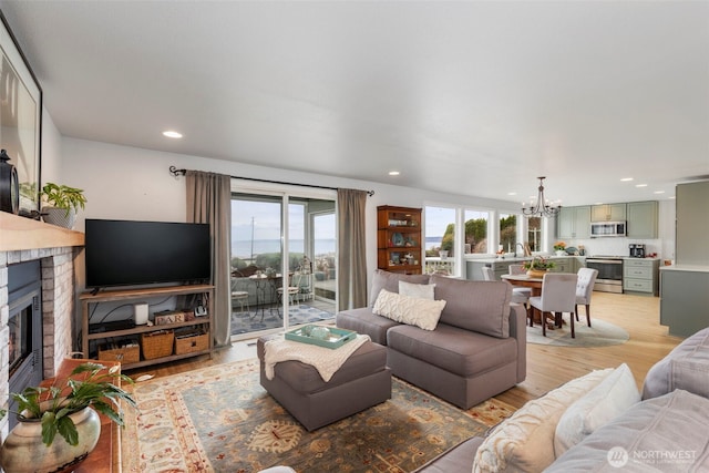 living room featuring a chandelier, a glass covered fireplace, light wood-style flooring, and recessed lighting
