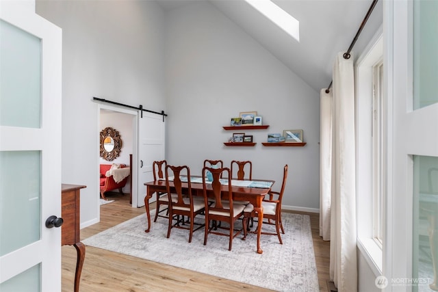 dining area with wood finished floors, baseboards, vaulted ceiling, and a barn door
