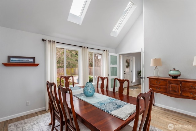 dining space with high vaulted ceiling, light wood-style flooring, baseboards, and a skylight