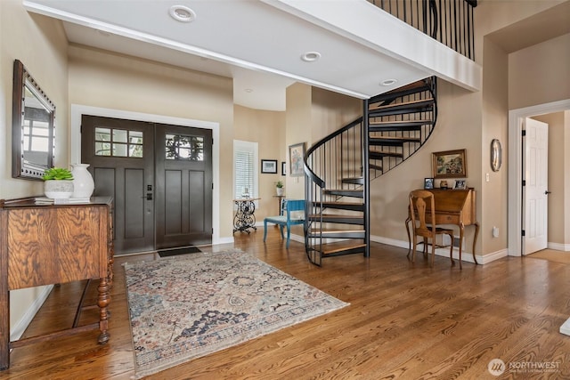 foyer entrance with a high ceiling, stairs, baseboards, and wood finished floors