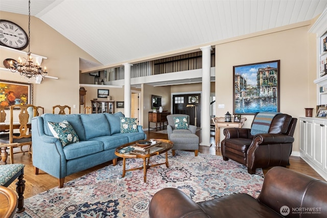 living area with high vaulted ceiling, a notable chandelier, wood finished floors, and decorative columns