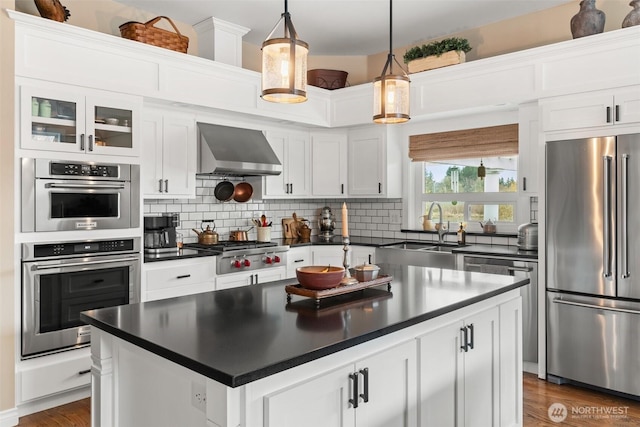 kitchen with dark countertops, stainless steel appliances, wall chimney exhaust hood, and a sink