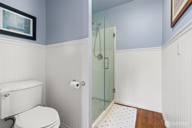 bathroom with a wainscoted wall, a shower stall, toilet, and wood finished floors