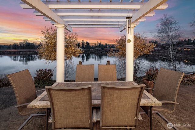 patio terrace at dusk with a pergola, outdoor dining area, and a water view