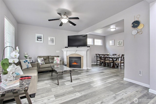 living area with a tiled fireplace, wood finished floors, a ceiling fan, and baseboards