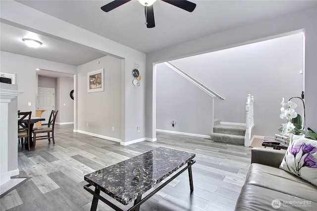 living area with stairs, baseboards, light wood-type flooring, and ceiling fan