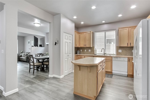 kitchen with light brown cabinetry, a sink, a center island, white appliances, and light countertops