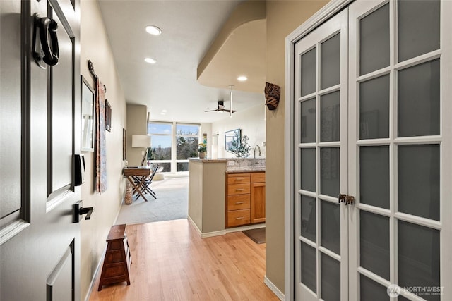 hallway featuring recessed lighting, baseboards, light wood finished floors, and a sink