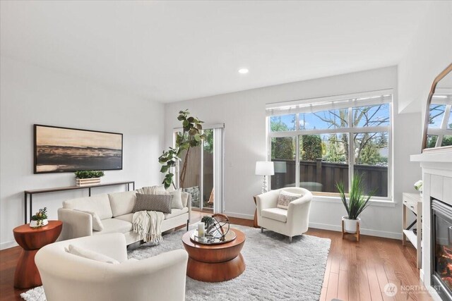 living room featuring a glass covered fireplace, recessed lighting, baseboards, and wood finished floors