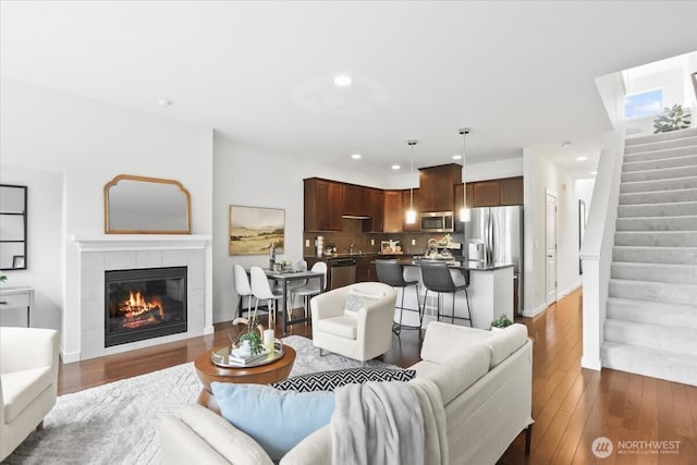 living area featuring recessed lighting, dark wood-style floors, stairs, and a tile fireplace