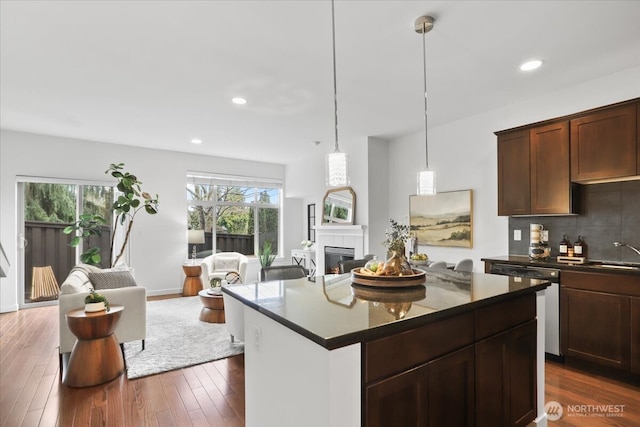 kitchen with dark countertops, a warm lit fireplace, dark wood-style floors, open floor plan, and dishwasher