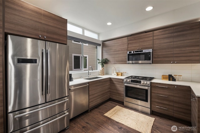 kitchen with backsplash, light countertops, appliances with stainless steel finishes, dark wood-style floors, and a sink